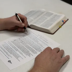 Hand completing a sermon preparation worksheet beside an open Bible