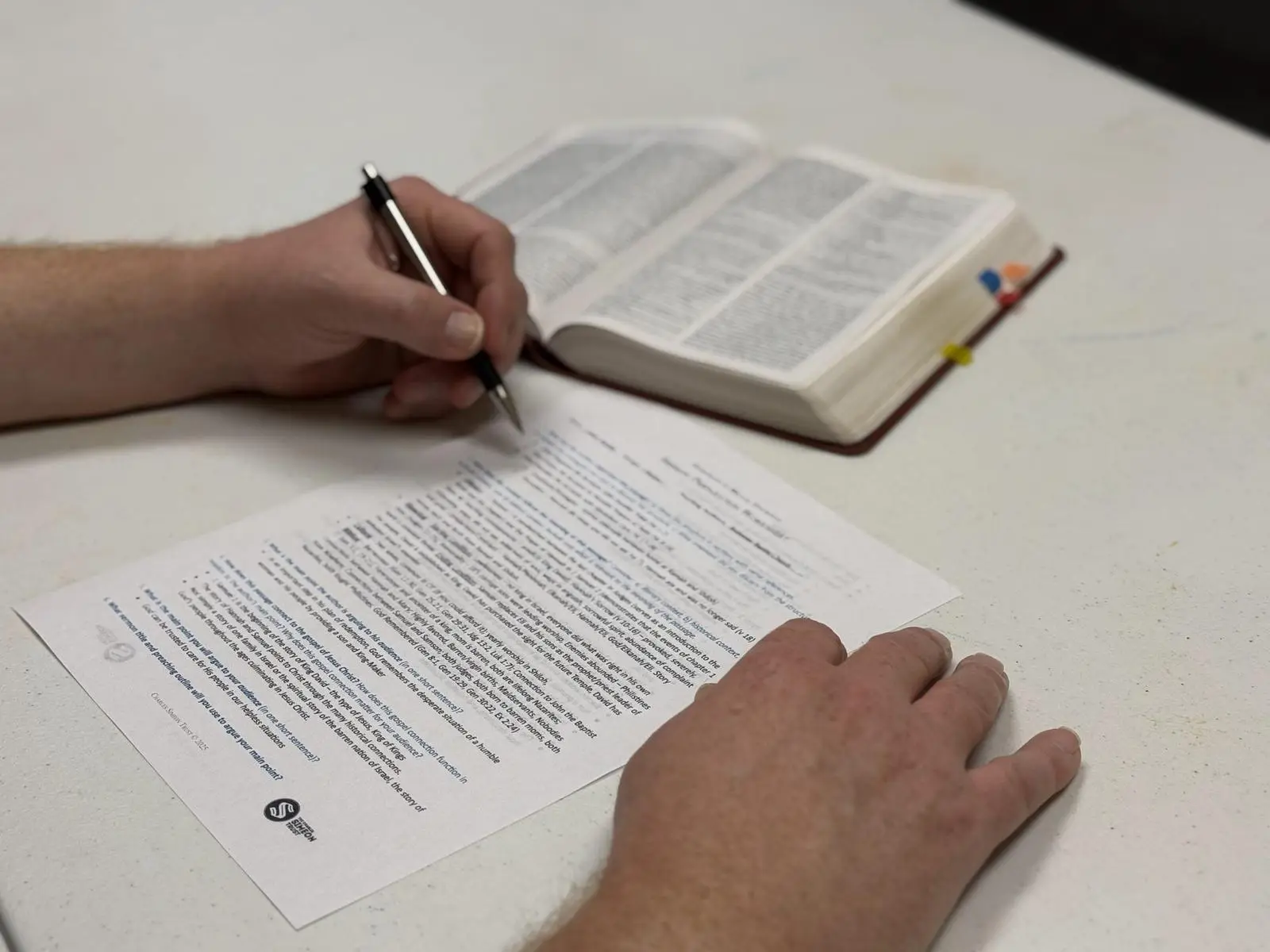 Hand completing a sermon preparation worksheet beside an open Bible
